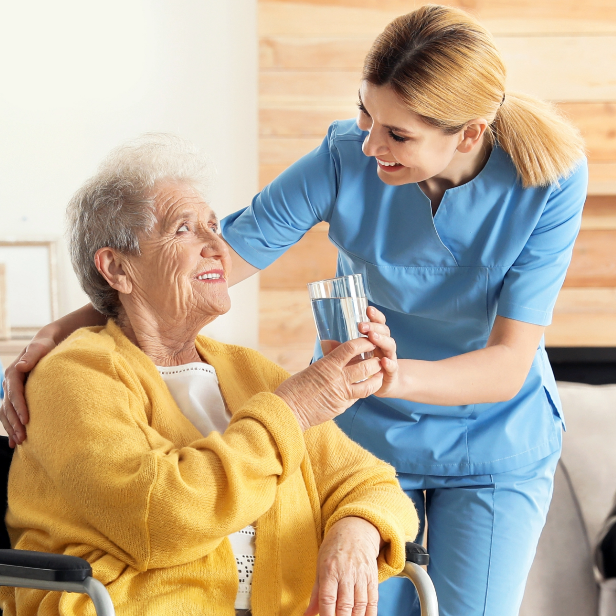 A carer giving water to a lady sitting down on a wheelchair