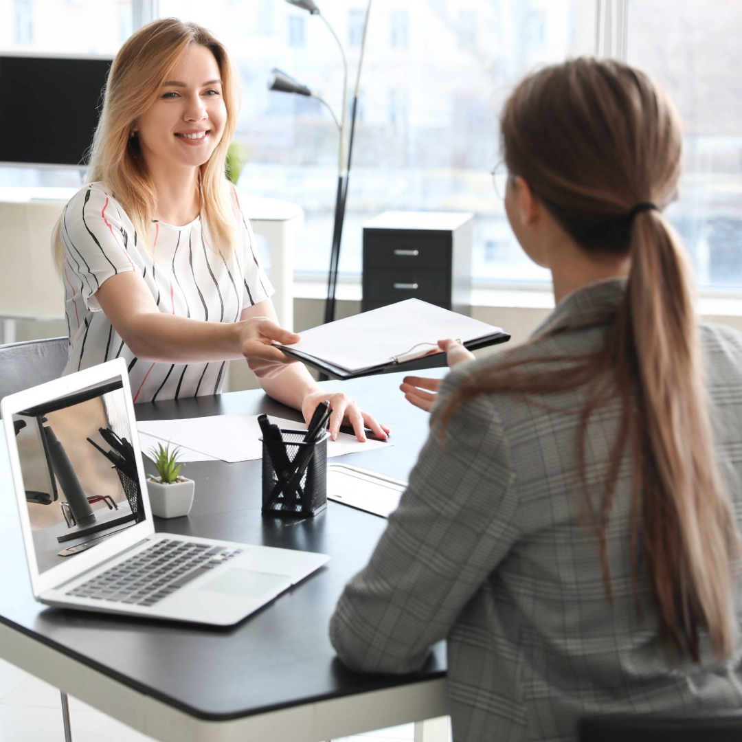 a women handing over a file to another women in a office setting
