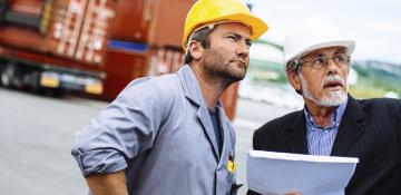 Two men looking to the sky wearing hard hats