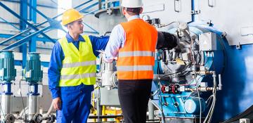 Two men with high visibility jackets looking at heavy machinery