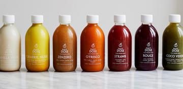 Image shows line of juice bottles from the brand Daily Dose. They go from left to right: white, yellow, orange, red, purple and green in different vegetable and fruit flavours.