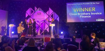 Image shows an awards stage with two men and one woman on stage receiving an award for 'Alternative Finance Provider of the Year' screen shows Close Brothers Invoice Finance 