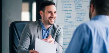 Two men in business attire smiling in a boardroom while looking at a piece of paper